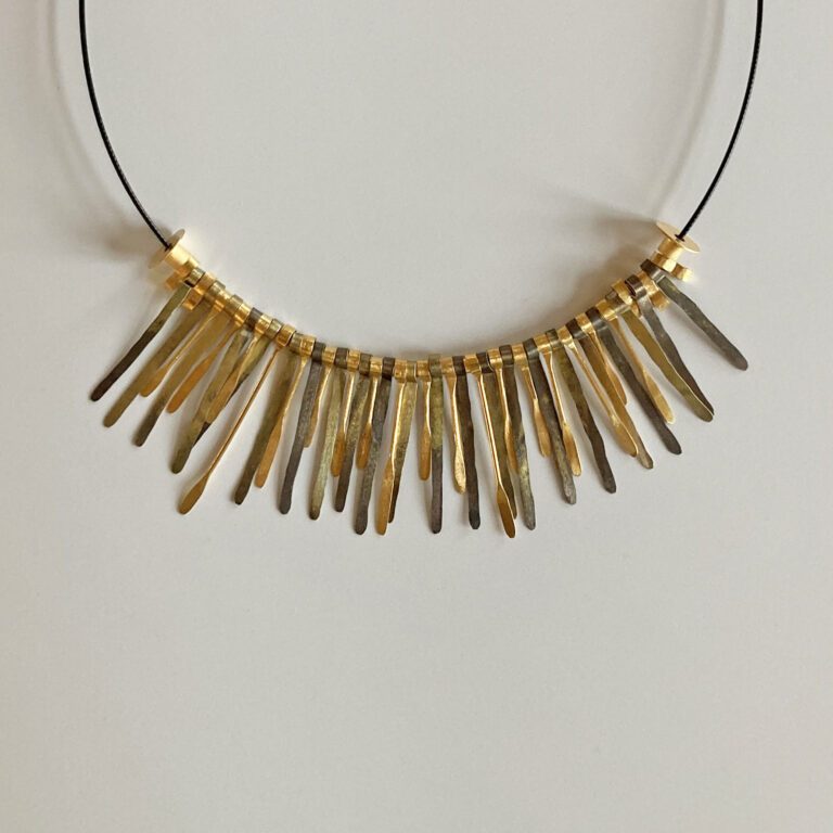 Kette mit unregelmäßigen, goldfarbenen Metallstäben an einem dünnen schwarzen Band